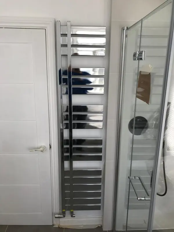 Tall chrome towel radiator beside a shower