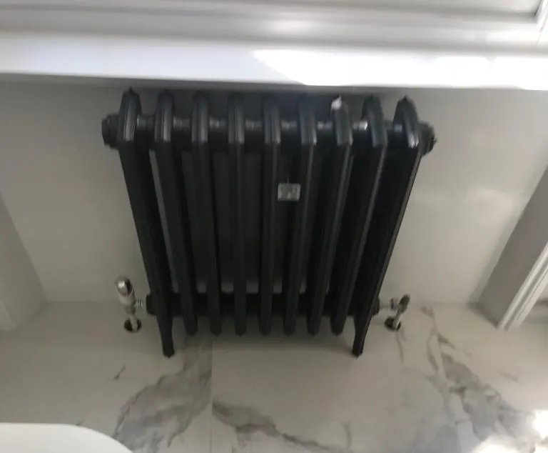 Black cast iron column radiator in a marble tiled bathroom