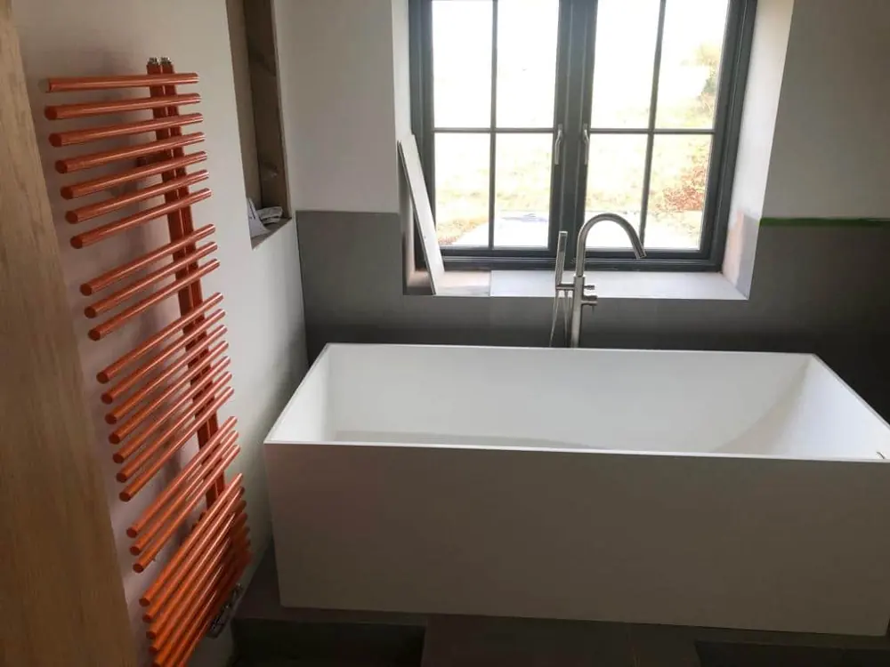 Freestanding bath under a window with an orange towel rail