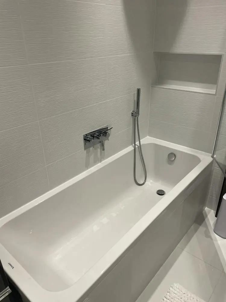 Bath with wall mounted shower controls and a tiled niche