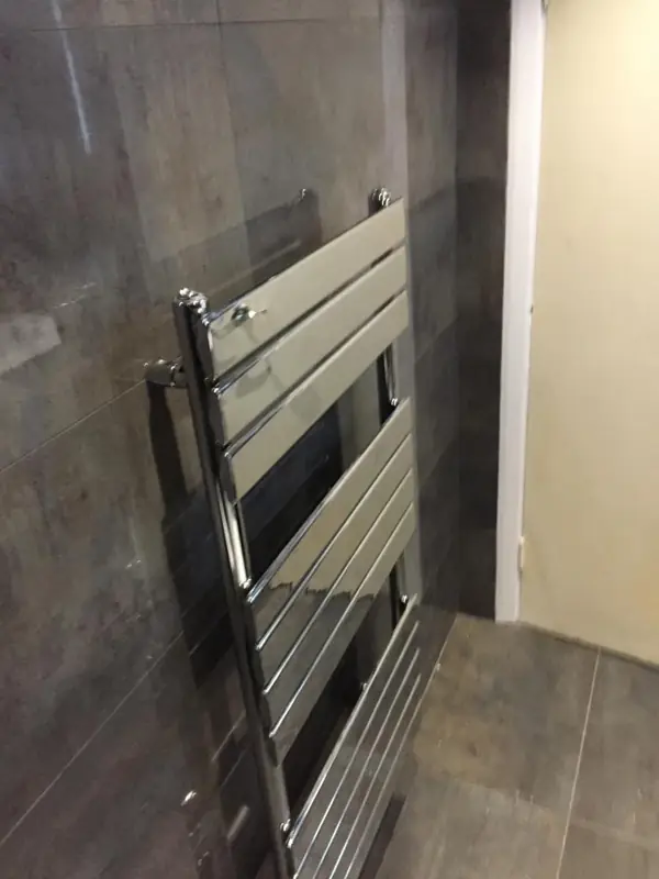 Chrome towel radiator on a dark tiled wall