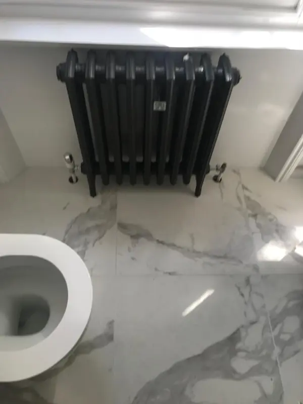 Black cast iron column radiator in a marble bathroom